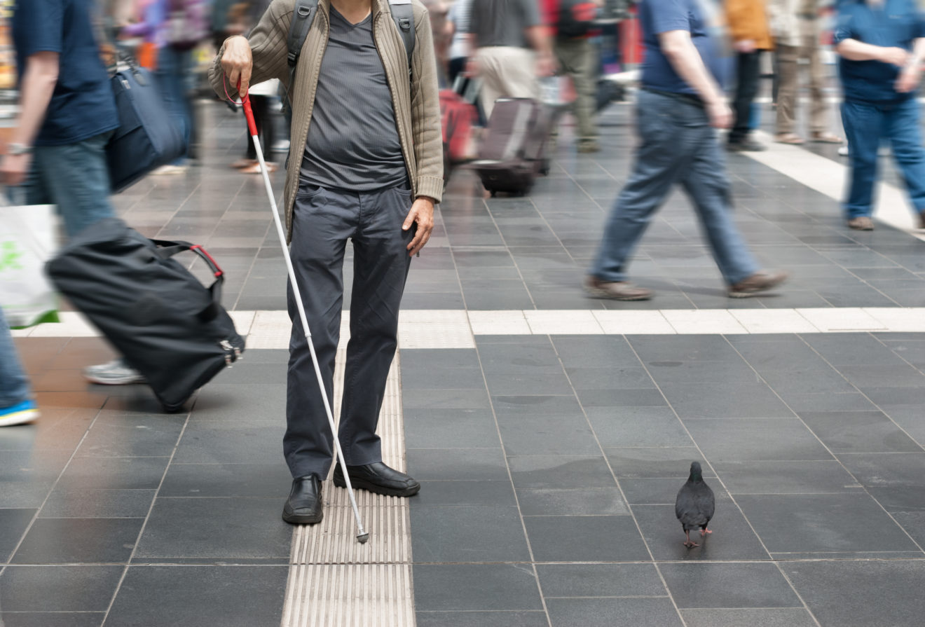 Image d'un homme malvoyant avec une canne suivant un dispositif au sol pour s'orienter.